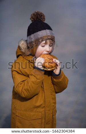 Cute baby boy funny eating fast food Burger on the street. Concept: city food, children's food.