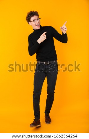 Image of young excited man in eyeglasses pointing fingers aside isolated over yellow background