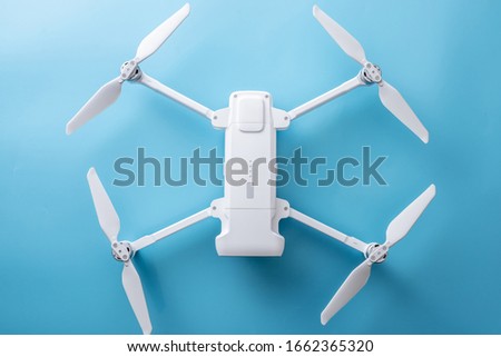 White folding quadrocopter drone with blades spread out on a blue background. Top view.