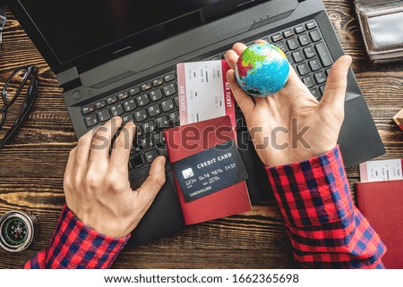 Preparing for an exciting journey. Man books flights by typing on a laptop and paying with a credit card on a wooden background. The view from the top.