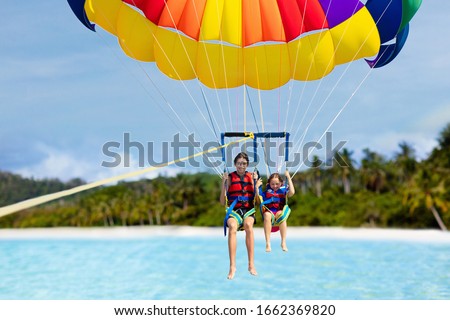 Kids parasailing. Water sport on summer vacation. Brother and sister flying in tropical ocean resort. Sea and beach fun. Rainbow parachute. Teenage boy and little girl fly. Royalty-Free Stock Photo #1662369820