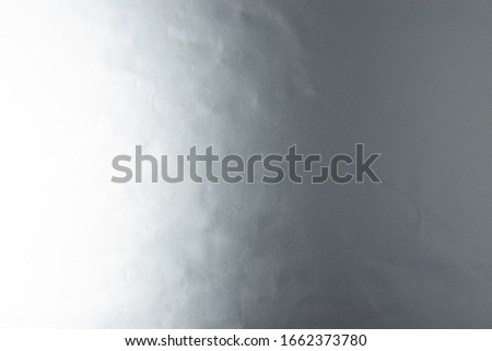 Silver background of real silver paper, illuminated by a soft light from the left, slightly creased.