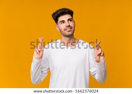 Young man over isolated orange background with fingers crossing and wishing the best