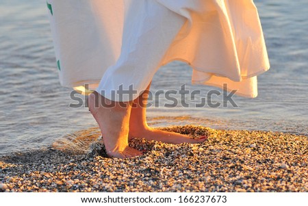Beautiful girl dancing on the beach in sunset light. Girl with beautiful legs entering the sea close up. Sunbathing in the seaside. Girl walking on beach. Summer vacation relaxation holiday on sea.