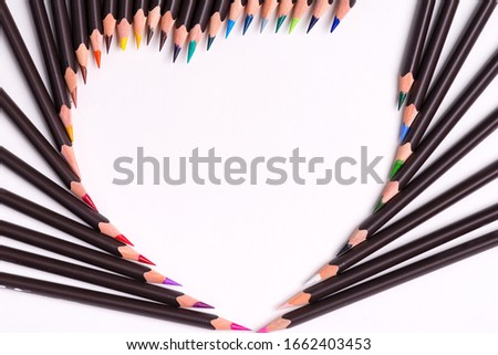 Creative backdrop from colorful pencils in the shape of heart on a white background. Flat lay.