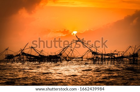 Traditional square fishnet at sunrise, Pakpra Canal, Phatthalung, Thailand, amazing orange cloudy sky at sunrise in Thailand with fishnet silhouettes