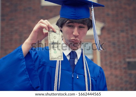 A closeup shot of a male graduate student in a blue mantle holding a one dollar bill - student unemployment concept