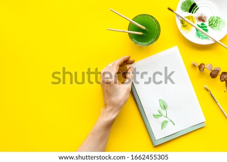 Painting. Female hands draw herbs on yellow background top-down copy space