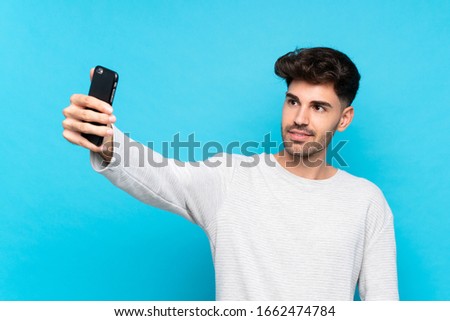 Young man over isolated blue background making a selfie