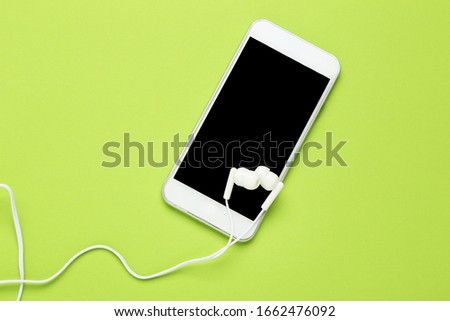 Earphones with mobile phone on green background