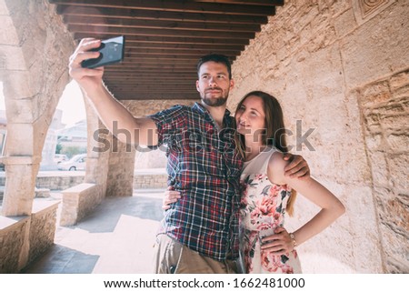 A young couple of lovers take a selfie against the background of an ancient temple or castle. A man hugs a girl and takes a photo near the ancient stone walls of the church