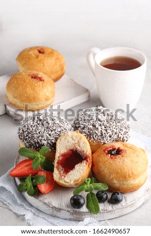 Dessert. Hanukkah doughnuts. Sweets for tea. Donuts with jam and chocolate on a light board. Blueberries, strawberries and mint with a cup of tea. Background image, copy space