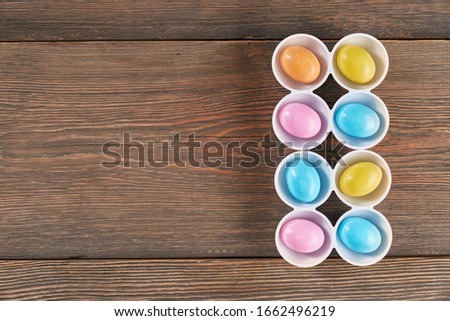From above view of eight colorful easter eggs in white cups isolated on wooden background. Process of coloring boiled food in different colors. Concept of spring and easter holidays.