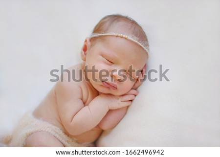 Close-up beautiful sleeping baby girl. Newborn baby girl, asleep on a blanket. A portrait of a beautiful, seven day old, newborn baby girl wearing a white fabric headband with flowers. Closeup photo