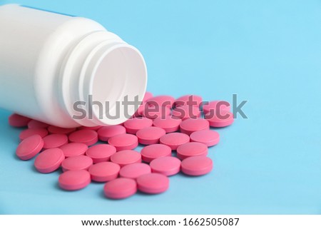 Group of pink round medicine pills and white bottle on a blue background. Selective focus. Theme of health care, medical treatment and disease prevention.