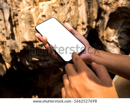 Mockup image hand holding black mobile phone with blank white screen at mountain cave. feeling relax and rest.