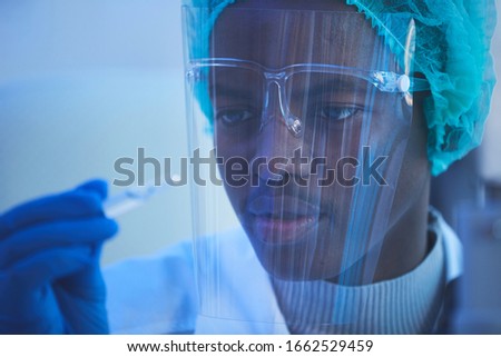 Horizontal close up portrait of young African American male laboratory scientist holding ampoule with new vaccine he developed