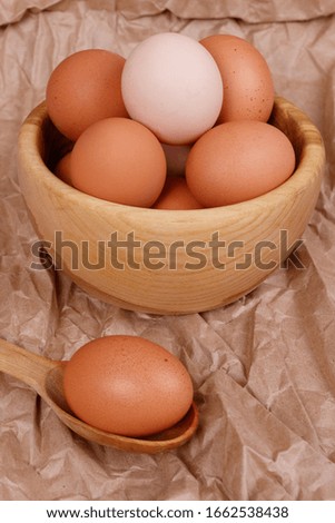 Yellow, beige and white chicken eggs in a wooden plate, one egg in a spoon. Kraft paper background.