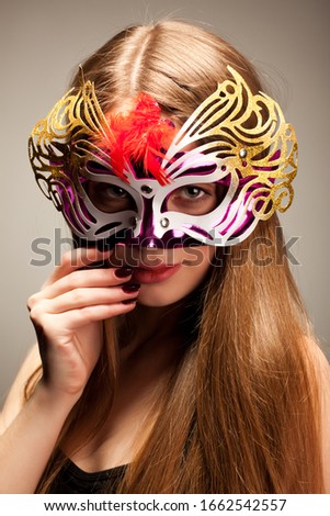 Seductive woman in large multicolored carnival mask, looking in camera, stroking her lower lip with her finger