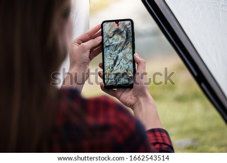 Women hands holding smartphone with app navigation hiking map on screen.  Mountains map with route and markers. Girl planning a trip inside the tent at the camp.  Royalty-Free Stock Photo #1662543514