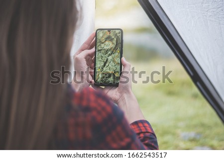 Women hands holding smartphone with app navigation hiking map on screen.  Mountains map with route and markers. Girl planning a trip inside the tent at the camp.  Royalty-Free Stock Photo #1662543517