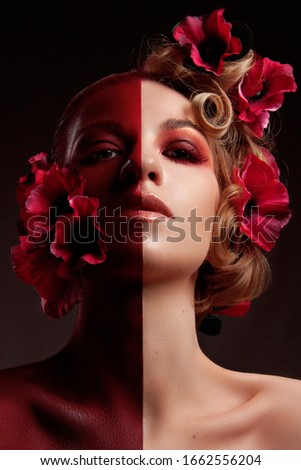 Beautiful creative photo of attractive girl with bright make up and red flowers in hair.
