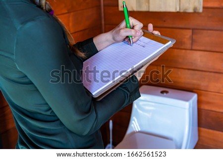 Woman construction inspector inspecting a house bathroom. close up, selective focus on her clipboard as she writes notes with toilet in the background