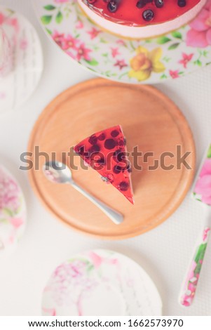 Blackberry cheesecake slice and spoon on round wooden board. Two cups for tea, saucer on white table. Cheese cake with black berries. Top view