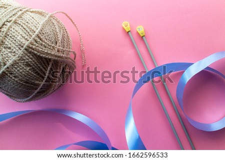 Knitting needles, wool yarn ball and ribbon on a plain pink background. Isolated with blank space to add text.