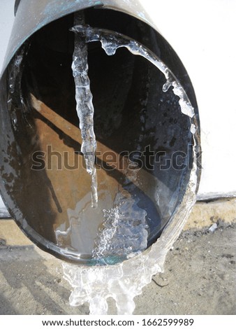 Frozen gutter hole with icicles, close up.