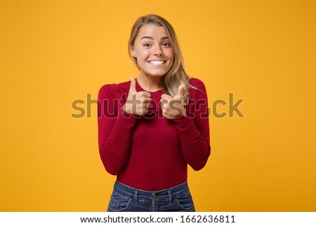 Smiling young blonde woman girl in casual clothes posing isolated on yellow orange wall background studio portrait. People sincere emotions lifestyle concept. Mock up copy space. Showing thumbs up