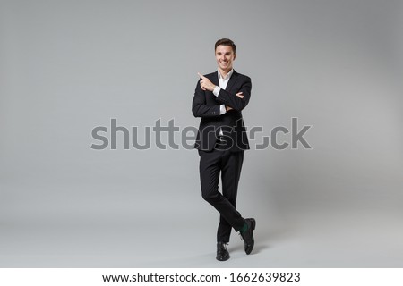 Cheerful young business man in classic black suit shirt posing isolated on grey background studio portrait. Achievement career wealth business concept. Mock up copy space. Pointing index finger up Royalty-Free Stock Photo #1662639823