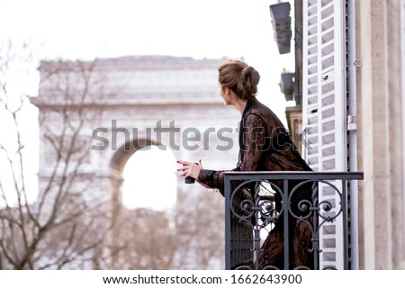 Attractive  yang woman in pajama is drinking coffee on balcony in the morning in city Paris. view of the triumphal arch.