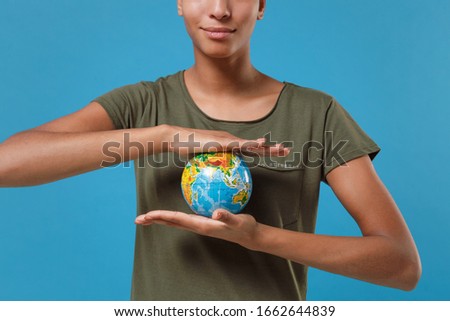 Cropped image of young african american woman girl in casual t-shirt posing isolated on blue background studio portrait. People emotions lifestyle concept. Mock up copy space. Hold Earth world globe