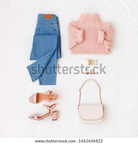Blue jeans, pink knitted sweater, heeled sandals and small bag with chain strap on white background. Overhead view of woman's casual outfit. Trendy stylish look. Women clothes. Flat lay, top view. Royalty-Free Stock Photo #1662646822
