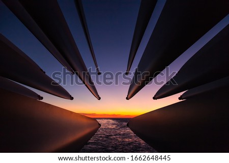 Transportation of blades of wind generators across the ocean. The blades stick out from the stern of the ship at sunset.