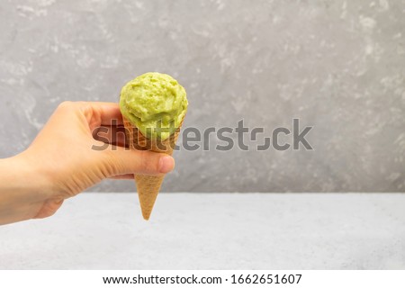 Woman hand holding a waffle cone with healthy homemade avocado ice cream on neutral background with copy space