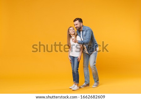 Excited bearded man in casual clothes have fun with child baby girl. Father little kid daughter isolated on yellow background. Love family parenthood childhood concept. Pointing index finger aside