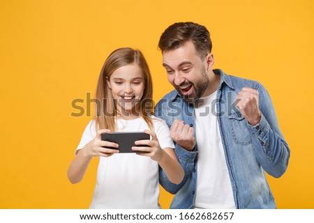 Funny bearded man with cute child baby girl. Father little kid daughter isolated on yellow background. Love family day parenthood childhood concept. Play game with mobile phone, doing winner gesture