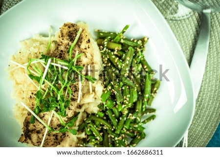 steak of halibut on puree with green beans and sesame. plate covered, ready to eat. top view