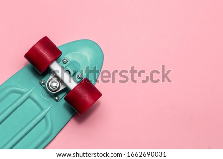 Green skateboard cruiser with red wheels on a pink background with copy-space