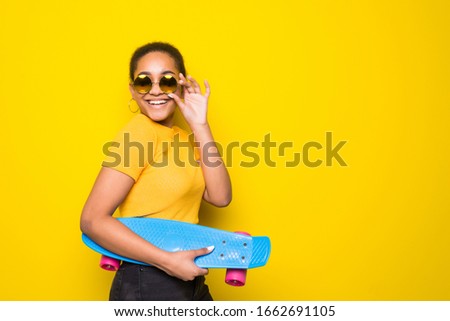 Portrait of latin young woman holding yellow skateboard isolated on yellow orange background. People lifestyle concept.