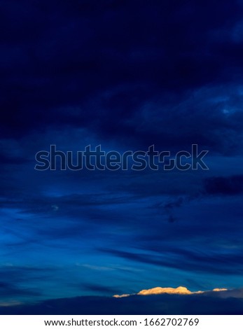 Vertical vivid blue nightscape of dramatic layered blues, pale moon and small bright cloud accent. Royalty-Free Stock Photo #1662702769