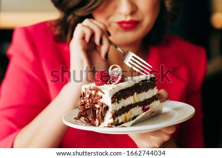 Close up image of woman eating cake Black Forest decorated with white chocolate and raspeberries
