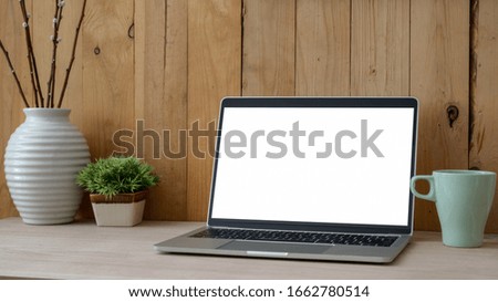 Cropped shot of simple workplace with blank screen laptop, mug and decorations on wooden table with plank wall background