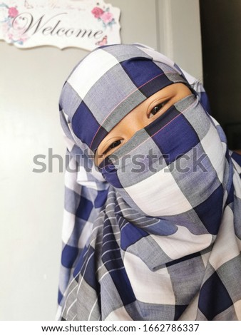 A portrait of a muslim young girl in niqab. She is smiling by looking at her eyes. 