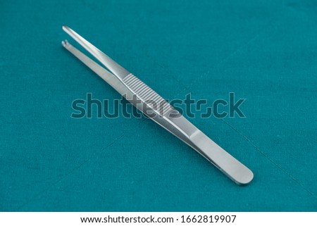 Basic surgical instrument stainless steel tissue forceps isolated on surgical green drape fabric