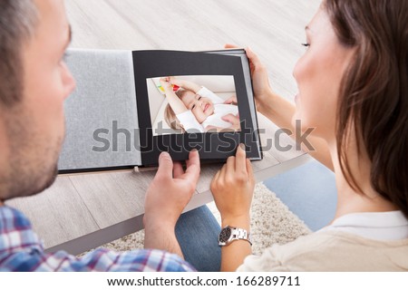 Young Couple Sitting Side By Side Looking At Baby's Photo