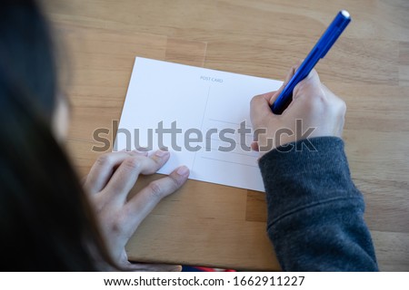 View of woman writing message on blank postcard for send back to home. Royalty-Free Stock Photo #1662911227