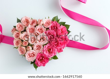 beautiful pink flowers in a heart- shaped box, pink ribbon, on a white table close-up with a blurred background, top view, as a background for the designer on a greeting card on March 8